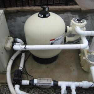 Salt System - Sunwave Pool Pros - Sunwave Pool Pros Pool equipment on a concrete pad including a round tan sand filter, pump, and PVC piping.